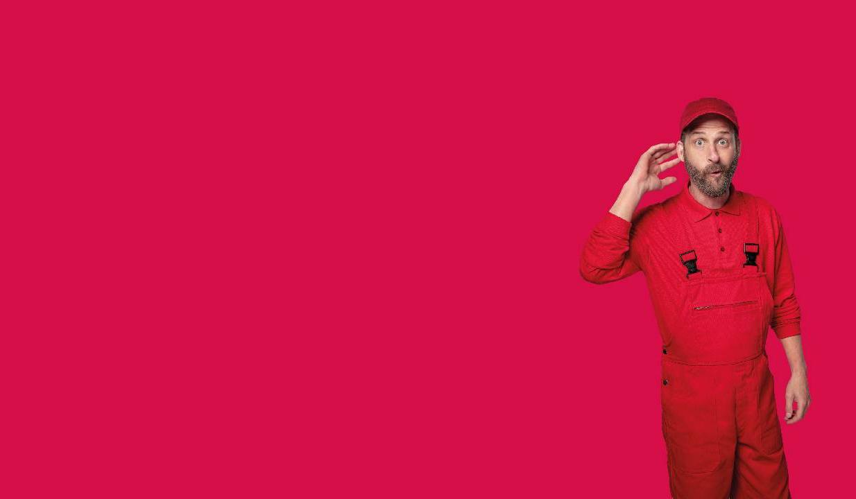 Bärtiger Mann in roter Arbeitskleidung in lauschender Pose vor neutralem Hintergrund in magenta