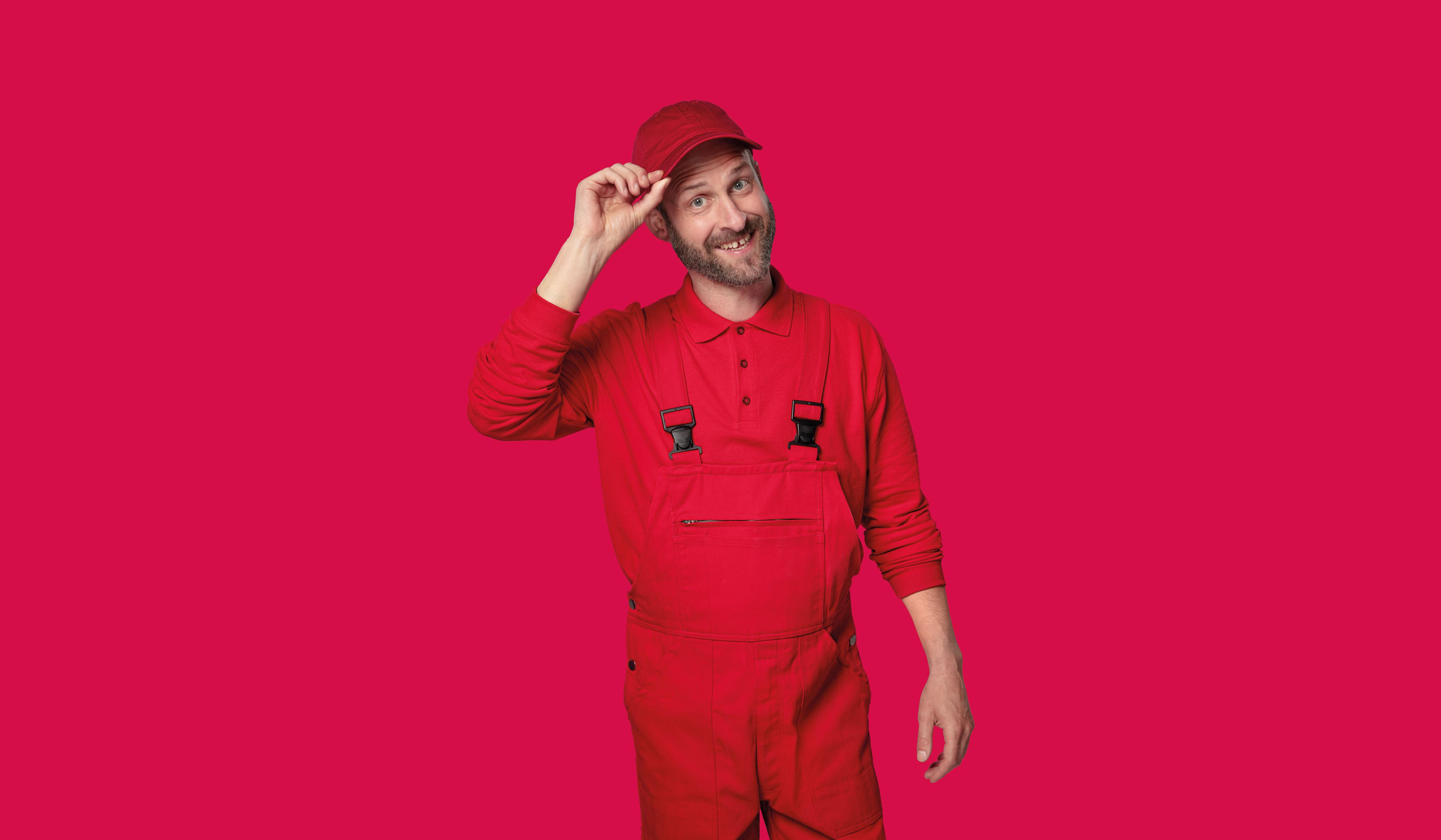 Mann in roter Arbeitskleidung lächelt vor knallrotem Hintergrund.